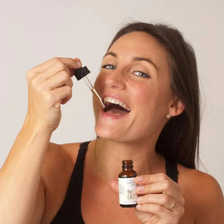 Woman holding a dropper near her mouth in a bathroom